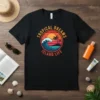 Black t-shirt with "Tropical Dreams Island Life" text, featuring a sunset, ocean wave, palm trees, and island graphic