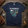 Navy t-shirt with white text "tu manera" and a graphic of a dove flying through clouds and stylized shapes