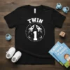 Black t-shirt with "Twin 1" text and two rockets in a circle graphic, designed for babies and toddlers