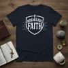 Navy t-shirt with white text reading "Unshakeable Faith" inside a shield graphic, with a cross at the top