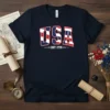 Navy blue t-shirt with bold red, white, and blue USA EST. 1776 graphic, symbolizing American patriotism and founding year