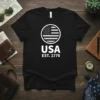 Black t-shirt with white USA EST. 1776 design featuring a circular American flag graphic above bold text