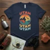 Retro "Utah Utah Utah" text with a circular graphic of mountains and a river, on a navy t-shirt
