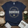 Navy blue t-shirt with "VERY DEMURE" text in white and gold, surrounded by a floral wreath and a coffee cup