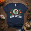 Navy t-shirt with "VIVA MEXICO" text, Mexican flag emblem, festive papel picado, and floral accents