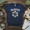 Navy blue t-shirt with "VOLUNTEER" text and a circular graphic of diverse hands planting a green seedling