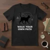 Black t-shirt with white text "WALK YOUR OWN PATH" and a black cat graphic surrounded by abstract lines and shapes