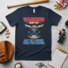 T-shirt with text "WARNING GAME DAY MAY BE LOUDER THAN THE UMPIRE" featuring a cartoon umpire graphic