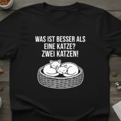 WAS IST BESSER ALS EINE KATZE? ZWEI KATZEN! text with two sleeping cats in a basket graphic on a black