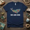 Navy blue t-shirt with "WE ARE ONE" text and a whale graphic made of colorful fish, representing unity and marine