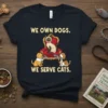T-shirt with "WE OWN DOGS. WE SERVE CATS." text featuring a regal cat on a throne served by two dogs