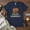 Welcome To The Snorefeast t-shirt design featuring a sleeping bear in an armchair with a small dog, text in cream