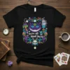 Black t-shirt with a circular design featuring the Cheshire Cat, mushrooms, teacups, and the quote "we're all mad here."