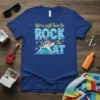 T-shirt with the text "We're Just Here To ROCK the AT" featuring a cartoon boat on waves, music notes, and