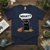 Black cat with arms crossed and a spilled plant pot, with "WHAT?" in a speech bubble, on a navy t-shirt