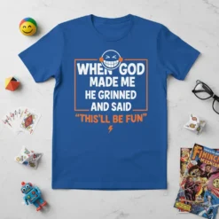 Blue t-shirt with white and orange text reading "When God Made Me He Grinned And Said 'This'll Be Fun'", featuring