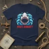 WHO'S HUNGRY? text with a fierce shark head graphic surrounded by ocean waves on a navy t-shirt