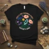 Black t-shirt with "WILD & FREE BLOOMING SPIRIT NATURE'S SONG" text and colorful floral illustration inside a green oval frame