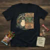 Black t-shirt featuring a raccoon at a "Will Trade Trade Post For Candy" stand, holding a backpack