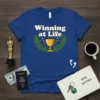 Winning at Life quote t-shirt with a gold trophy and laurel wreath graphic, white text with yellow outline
