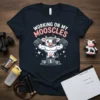 Working On My Mooscles t-shirt design with a muscular cow flexing on a winner's podium and stars