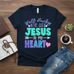 Navy t-shirt with colorful text reading "y'all Lucky I'VE GOT JESUS IN MY HEART" and small dove graphics, arrows, and