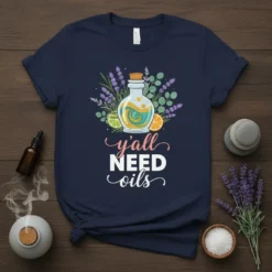 Navy t-shirt with "y'all NEED oils" text and a central graphic of a glass bottle filled with swirling oils, surrounded