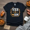Black t-shirt with "YES I AM" text in white and orange, featuring decorative brackets and a heart symbol