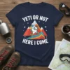 Yeti or Not Here I Come text with a cartoon Bigfoot hiking on mountains graphic, on a navy blue t-shirt
