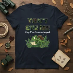 T-shirt design with camouflage text "YON'T SEE ME Cuz I'm Camouflaged" and a green chameleon wearing a backpack, holding a