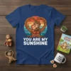 Two cartoon monkeys hugging inside a heart-shaped tree on a navy blue t-shirt with "YOU ARE MY SUNSHINE" text