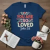 Christian t-shirt with "YOU ARE SO LOVED John 3:16" in red, pink, and cream text, adorned with hearts and decorative