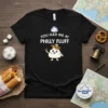 Black t-shirt with white text "YOU HAD ME AT PHILLY FLUFF" and a cartoon character holding a pretzel, wearing a