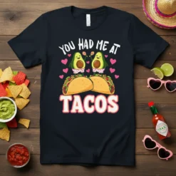 Cute "You Had Me At Tacos" t-shirt design with smiling avocados and tacos, surrounded by pink hearts