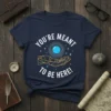 Navy t-shirt with white text "YOU'RE MEANT TO BE HERE!" and a graphic of a hand holding a blue orb