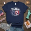'Merica 2021 design with American flag elements and fireworks on a navy blue t-shirt