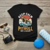 Keep Calm It's A Pitbull Not A Shark quote on a black t-shirt with a pitbull graphic on waves and