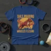 T-shirt design with text "TAILS WAGGING MUSCLES FLEXING" above a muscular pitbull flexing, set against a sunburst graphic and city