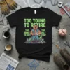 Black t-shirt with green text "Too Young to Retire" above a pitbull character holding a cup, with "Too Broke to